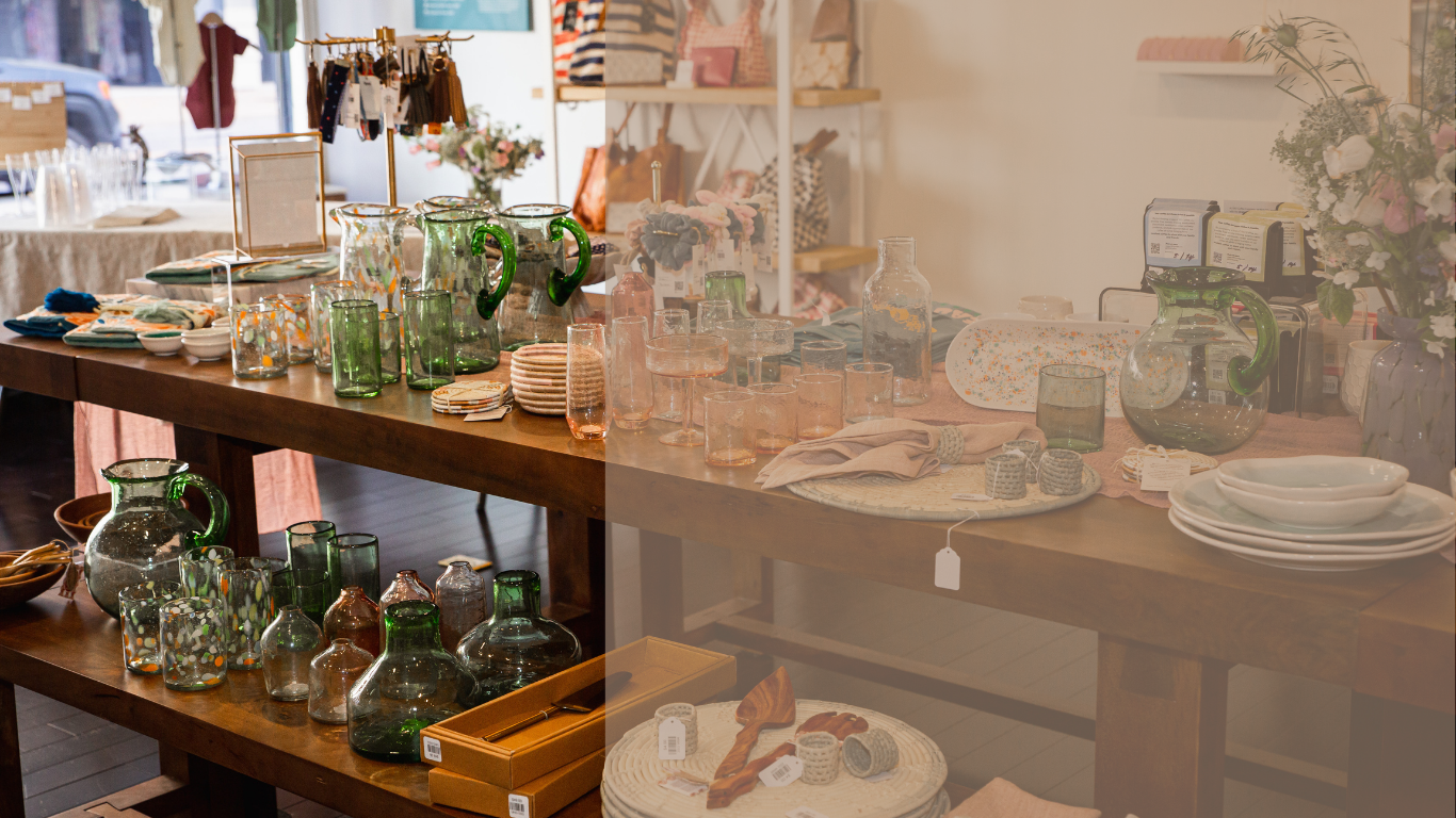 Long wooden table in retail store featuring glassware and dinnerware.