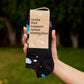 Black socks with space-themed design held by a hand against a blurred green outdoor background