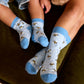 Two pairs of blue socks with bee pattern worn by children and adults on a dark surface.