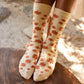 Feet of person wearing yellow crew socks with orange floral patterns on a blurred natural background