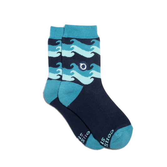 Three pairs of socks with ocean-themed design and 'socks that protect oceans' packaging by Oceana on a concrete surface near water.