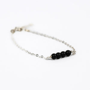 silver chain bracelet with four black onyx beads on a white background