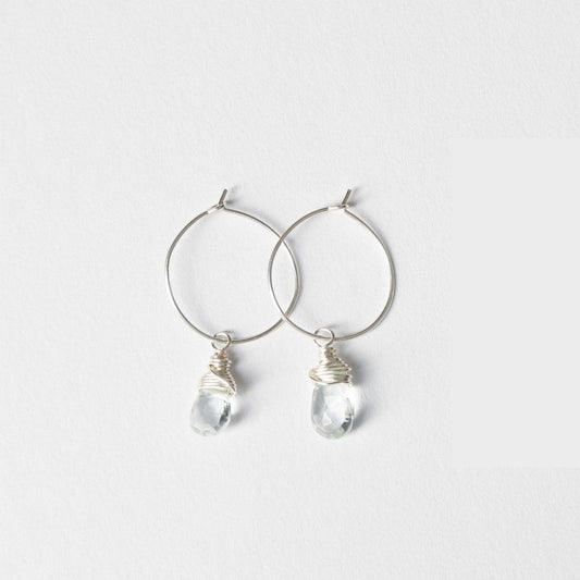 A woman in a blue and white striped top wearing the Mini-Hoop Aqua Quartz Charm Earrings in Sterling Silver, smiling and looking off to the side.
