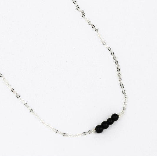 silver chain link necklace with four black onyx beads at the center on a whilte background