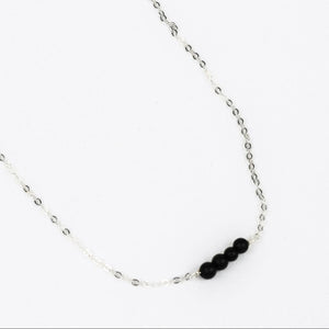 silver chain link necklace with four black onyx beads at the center on a whilte background