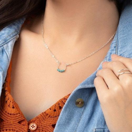A woman wearing a denim jacket and an orange top with geometric patterns, showcasing the Moab Western Beaded Necklace in sterling silver necklace with turquoise beads.