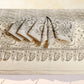 A folded textile set with a cream base and dark gray paisley and floral border pattern, displayed on a matching patterned surface against a light neutral background.