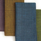Four folded woven fabric napkins or cloth squares in overlapping vertical rows, shown on a white background. The frontmost cloth is slate blue, with additional visible colors including olive green, mustard yellow, and dark purple.
