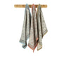 Three patterned kitchen towels hanging on a wooden rack against a white background