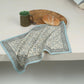 Patterned cloth on a surface with a mug, bread, and cutting board.