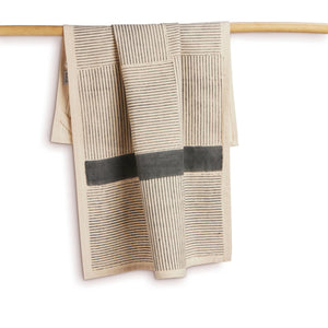 Textured towel with geometric pattern hanging on a wooden rod against a white background