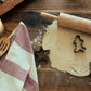 Baking setup with rolled-out dough, cookie cutters, and rolling pin on a wooden surface.