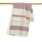 A striped kitchen towel in cream and dusty rose hanging from a wooden rod against a white background.