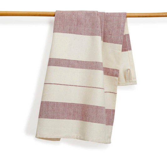 A striped kitchen towel or napkin in cream and dusty pink, laid diagonally on a wooden table with a small set of white measuring spoons resting on top.