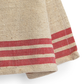 Close-up of a woven textile, likely a towel or blanket, in natural beige jute with bold red horizontal stripes near the bottom edge, shown on a white background.