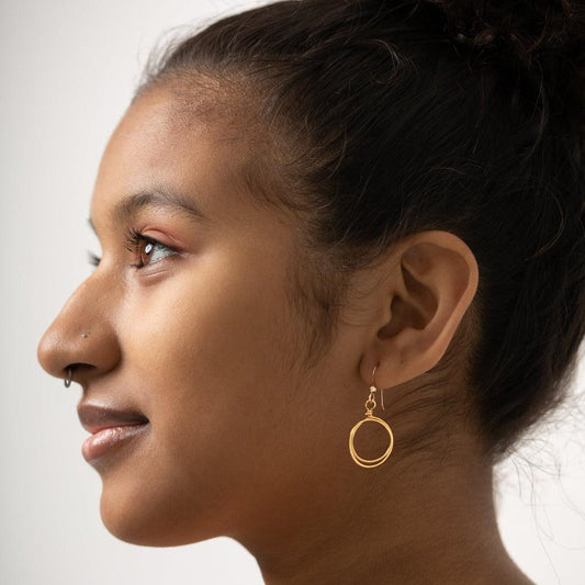 Sideview of young woman wearing Zomi Circles of Unity Earrings in 14k Gold Filled.  Earrings feature a double circle drop of hand-hammered brass.