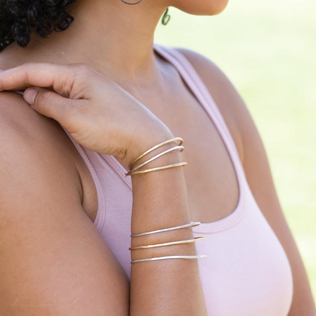 Woman's arm wearing stack of hammered bangles in sterling silver and brass.