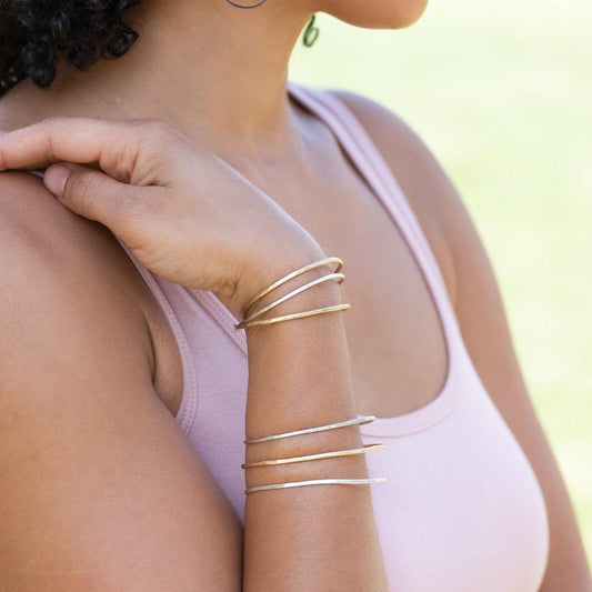 Woman's arm wearing stack of hammered bangles in sterling silver and brass.