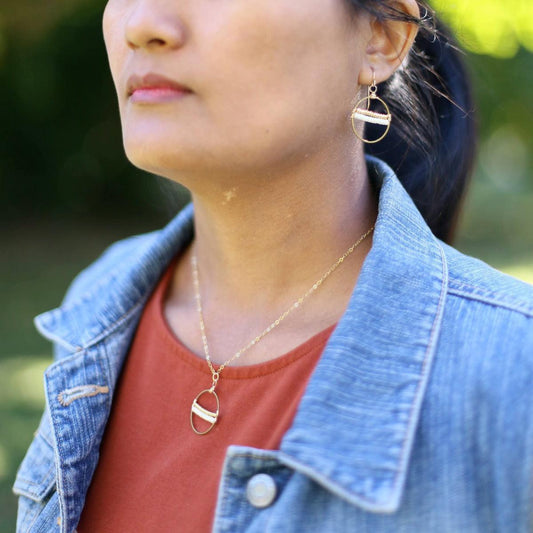 A woman wearing the Samira Seeds of Hope Necklace in 14k Gold Filled which features a brass circle with white and gold seed beads threaded across the center.