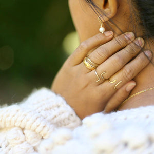 Hand of woman wearing Shanta Hand-hammered Ring in Brass on left hand with other rings.